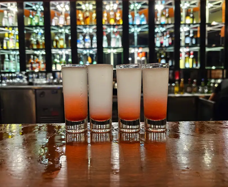 Vier Shots auf der Bar, dahinter beleuchtete Flaschenregale