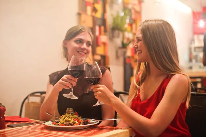 Zwei Freundinnen stoßen beim Abendessen mit Rotwein an